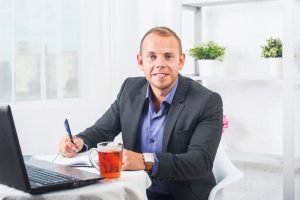 Businessman working in office, sitting at table with a laptop, looking smiling